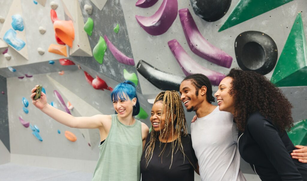 Group Of Multi-Cultural Friends Posing For Selfie By Climbing Wall At Indoor Activity Centre